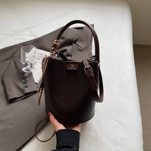 Detail der dunkelbraunen Leder-Eimertasche mit Seidentuchgriff auf grauem Blazer-Hintergrund