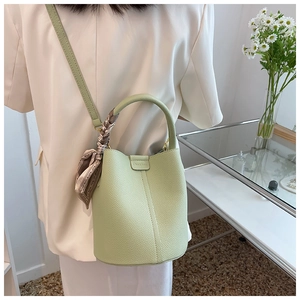 Detail of light green bucket bag with lychee texture and silk scarf handle on a glass table