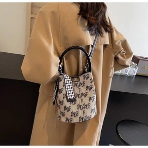 Detail der beigen Jacquard-Beuteltasche mit schwarzen Buchstaben und kariertem Seidenschal