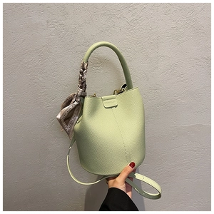 Detail of pistachio green bucket bag with lychee texture and silk scarf on handle