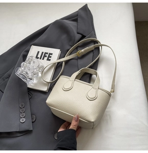 Detail of off-white lychee grain bucket bag with dual handles and slim shoulder strap