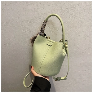 Close-up of light green lychee leather bucket bag with decorative silk scarf on the handle