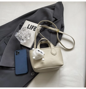 Detail of creamy white litchi grain leather bucket bag with cute plush pendant and strap