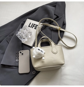 Detail of off-white lychee grain leather bucket bag with cute plush charm and gold hardware