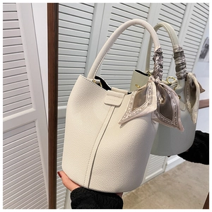 Detail of white lychee leather bucket bag featuring a decorative printed handle scarf