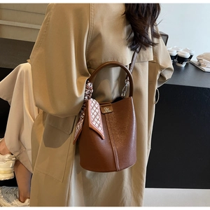 Detailansicht einer braunen Leder-Eimertasche mit dekorativem Tuch und Metall-Logo-Plakette
