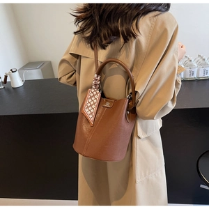 Detail einer braunen Eimer-Tasche aus Leder mit elegantem Rautenmuster-Schal am Griff