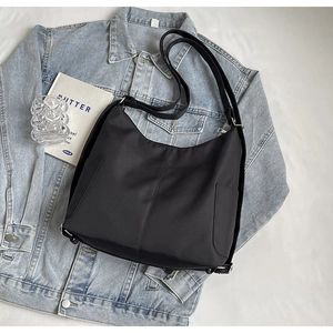 Detail van minimalistische zwarte hobo-tas met zijzakken op blauwe denim stof