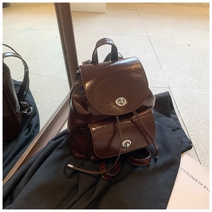 Detalle de la mochila de charol marrón oscuro con cierres plateados y diseño de cordón
