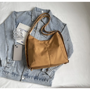 Bruine nylon hobo-schoudertas met dagelijkse accessoires en spijkerjasje op lichte achtergrond