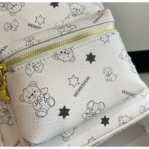 Detail der cremeweißen Ledertasche mit Bärendruck und goldfarbenem Metallreißverschluss
