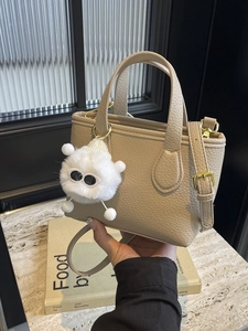 Chic beige textured bucket bag with plush monster charm and golden hardware