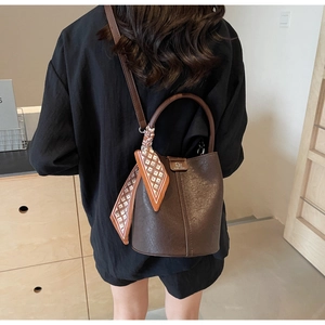 Detail der dunkelbraunen Leder-Eimertasche mit Tragegriff und Seidenschal-Accessoire