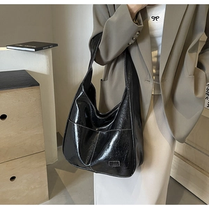 Detail of black glossy tote bag featuring contrast white stitching and metal logo tag