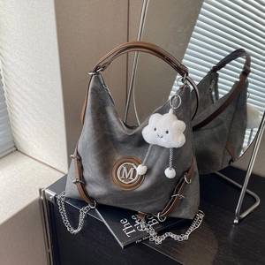 Detail of dark grey hobo bag with M-logo, plush cloud charm, and silver chain accent