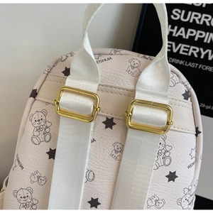 Detail eines cremefarbenen Rucksacks mit Cartoon-Prints, weißen Trägern und Gold-Schnallen