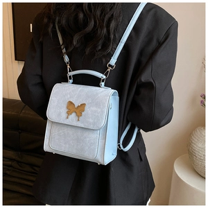 Vue détaillée d'un petit sac à dos bleu clair en cuir avec fermoir papillon doré sur un mannequin