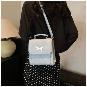 Détail du fermoir papillon argenté sur un sac à bandoulière en cuir mat bleu clair porté