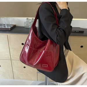 Close-up of a burgundy glossy leather hobo bag with a FASHION metal plaque detail