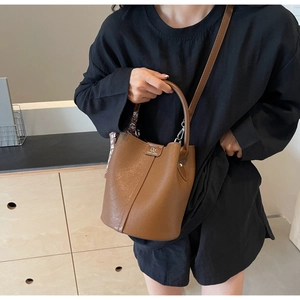 Detail einer braunen Eimer-Tasche aus Leder mit rundem Griff und Logo-Metallplakette