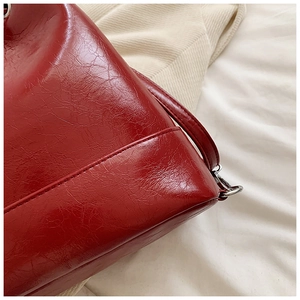 Dettaglio borsa a secchiello rossa lucida con trama vintage craquelé e cuciture precise