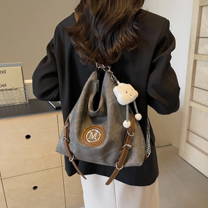 Detail of grey canvas backpack with metal M logo, leather straps and plush cloud charm