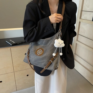 Detail of gray canvas shoulder bag with leather strap, metal chain, and plush pendant
