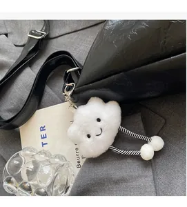 Détail du sac à bandoulière noir avec charm nuage en peluche blanc et motif visage souriant