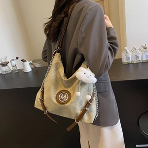 Detail of canvas tote bag with metal M logo, leather chain strap, and cloud charm
