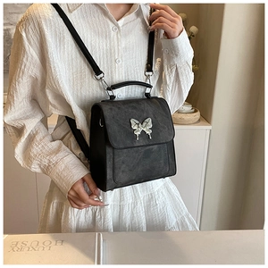 Détail d'un sac vintage en cuir noir mat avec un ornement de papillon en argent
