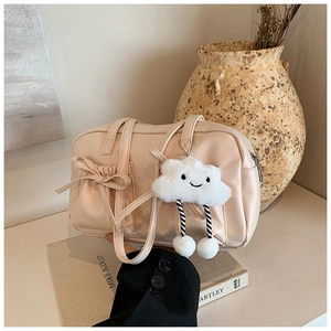 Detail of cream bowling bag with ribbon bow and plush cloud charm on white table