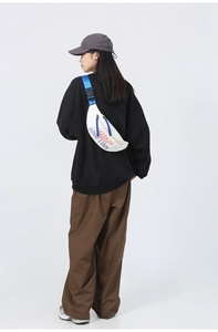 Rear view of model wearing white crossbody bag with blue straps and colorful text print