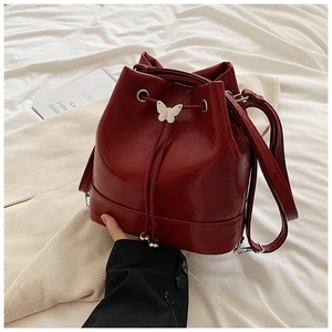 Dettaglio di una borsa a secchiello bordeaux con texture lucida e farfalla bianca