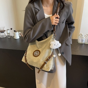 Detail of canvas tote with leather trim, metal M logo, and plush cloud charm accessory