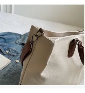 Close-up of beige nylon tote bag detailing brown leather trim and dark metal hardware hook