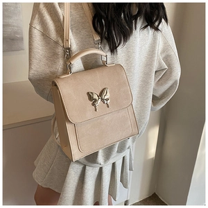 Détail d'un sac bandoulière carré abricot clair avec fermoir papillon argenté et texture cuir
