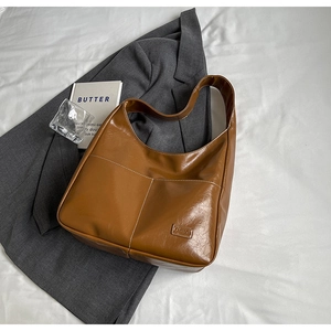 Detail of caramel brown tote bag featuring white contrast stitching and fashion tag