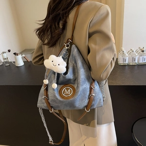 Blue denim hobo bag with M logo, brown leather handles, and white cloud plush charm