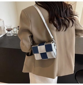 Detail of silver metallic and blue denim woven crossbody bag with slim strap on a model