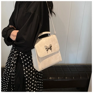 Sac à bandoulière chic blanc crème avec boucle papillon porté par un mannequin élégant