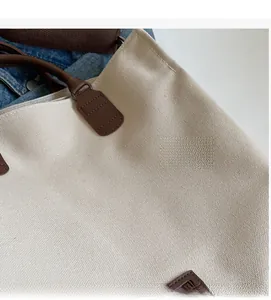 Close-up of durable beige canvas tote bag with premium brown leather strap and stitching