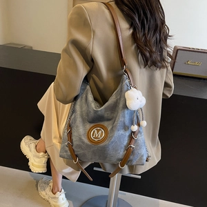 Detail of blue denim hobo bag with brown leather strap and plush cloud charm