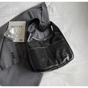 Minimalist black PU hobo shoulder bag with contrast stitching on a grey blazer suit