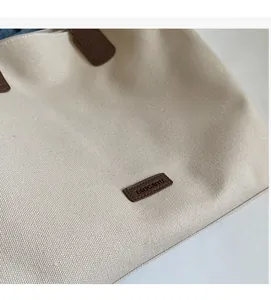 Close-up of leather logo patch and nylon fabric texture on a cream tote bag