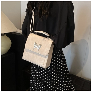 Détail du sac beige avec boucle papillon argentée porté à l'épaule par le mannequin