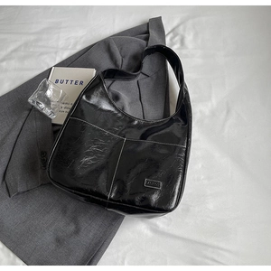 Detail of black patent leather hobo bag with contrast stitching and front pockets