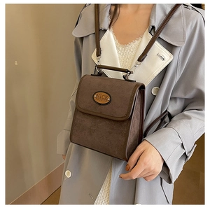 Close-up of brown suede crossbody bag featuring a metal plate and premium hardware details