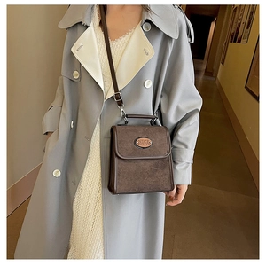 Detail of vintage brown suede crossbody bag featuring Nice Fashion logo on a long trench coat