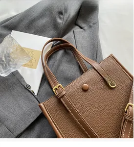 Nahaufnahme der braunen Handtasche mit Litschi-Maserung, verstellbaren Griffen und weißen Nähten