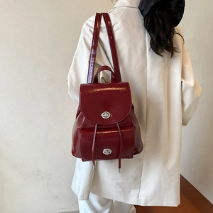 Detalle de mochila de charol granate con cierres de giro plateados sobre un traje blanco